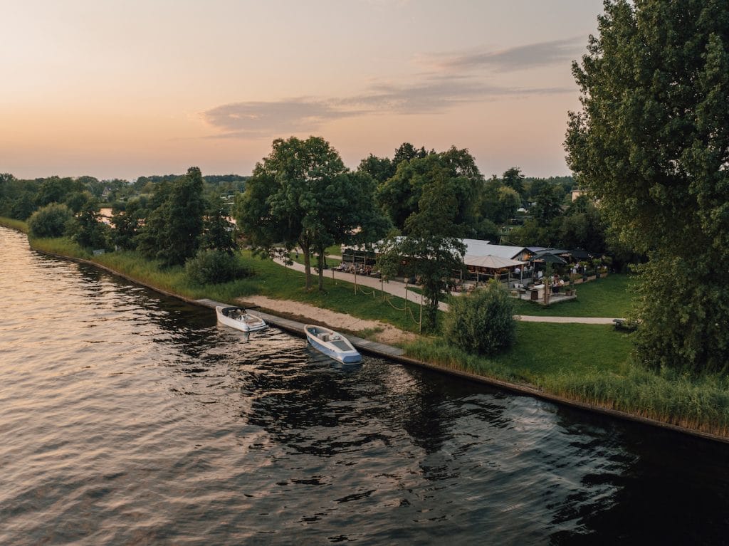 Restaurant aan het water - Dronefoto van restaurant aan het water in Vinkeveen met aanlegsteiger en groen terrein – Wander Island tijdens zonsondergang.